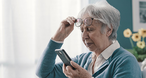 a woman lifting her glasses to squint as a mobile phone